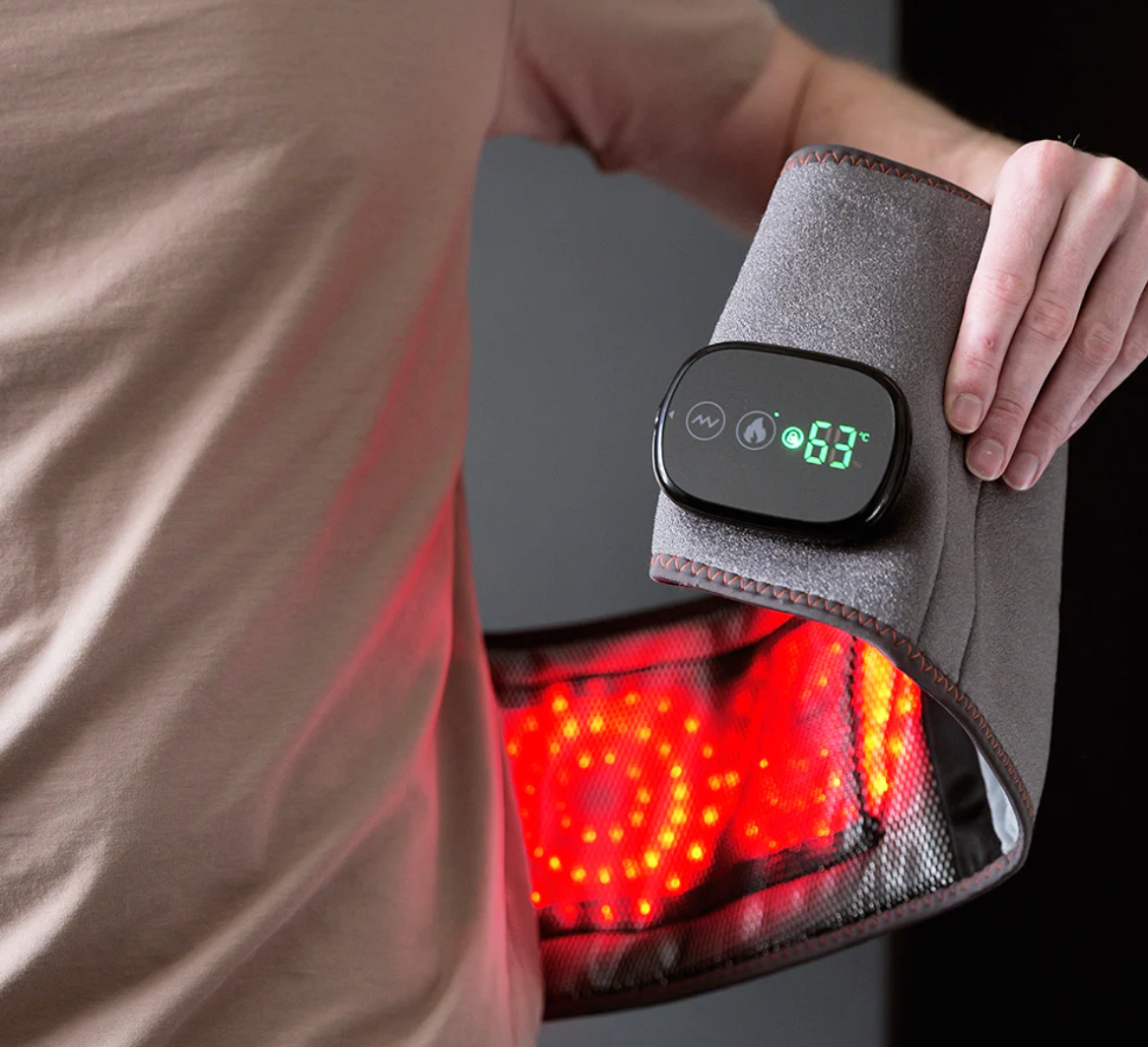 Bild eines tragbaren Rücken‑ und Wärmegürtels mit digitalem LED‑Display (63 °C), der um die Taille gelegt wird und rot leuchtende Infrarot‑Wärme an Rücken und Taille abgibt.